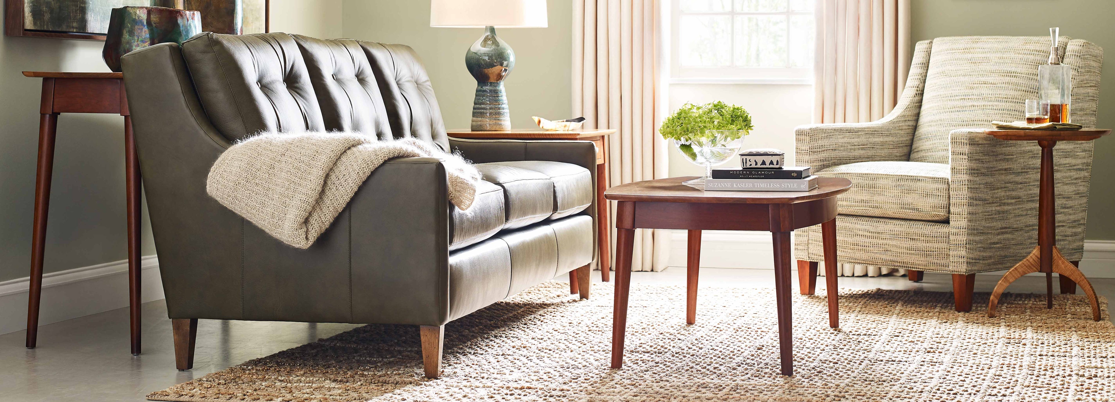 Lifestyle of a gray leather 500 Series Three Cushion Sofa with a cream throw blanket over the arm, there is a patterned fabric accent Chair next to it and a coffee table in front of both 