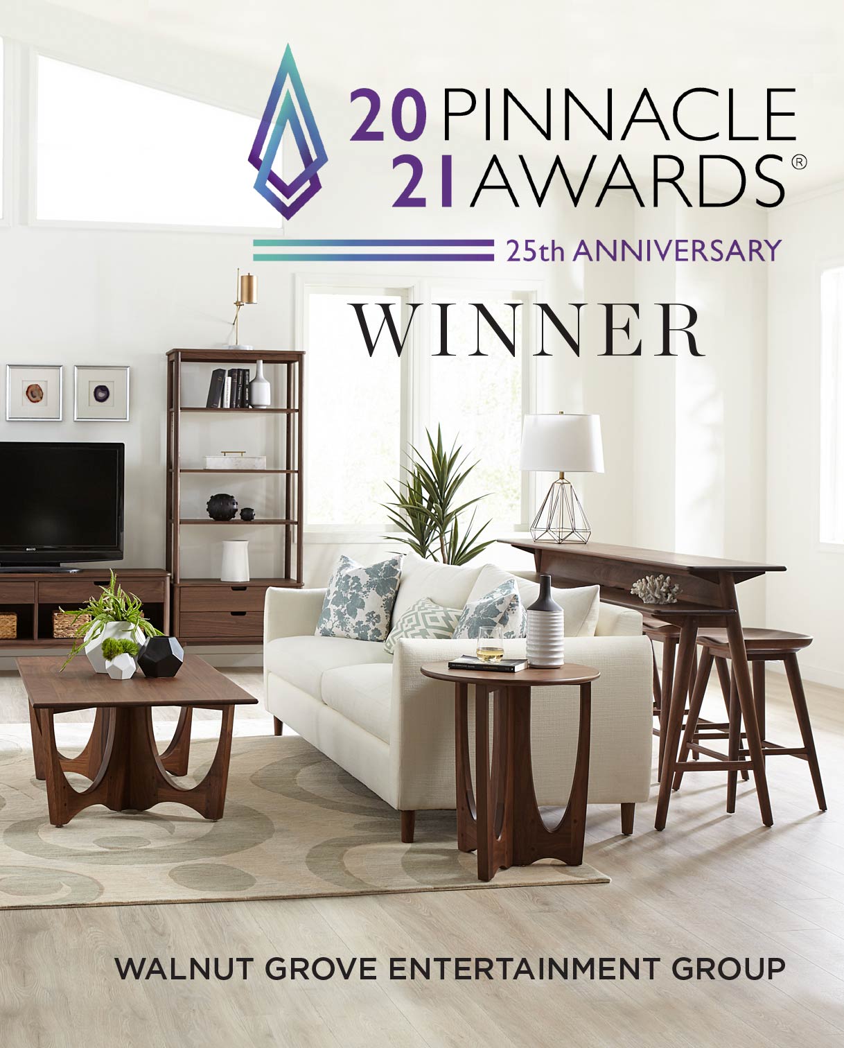 Pinnacle Awards® 2021 Winner image featuring the Walnut Grove Entertainment Group. The bright, modern living room includes a cream upholstered sofa, matching wood coffee and side tables with curved cutout bases, a TV console with shelving units, and a tall counter-height table with stools, all in rich walnut wood.