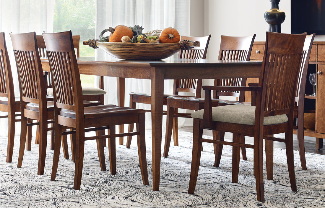 Origins by Stickley Gable Road dining set in a warm cherry finish, featuring a rectangular table surrounded by slat-back chairs with a mix of wood and upholstered seats. Styled with a fall-inspired centerpiece of pumpkins and gourds, the room exudes classic charm and casual elegance, perfect for seasonal gatherings and everyday dining.