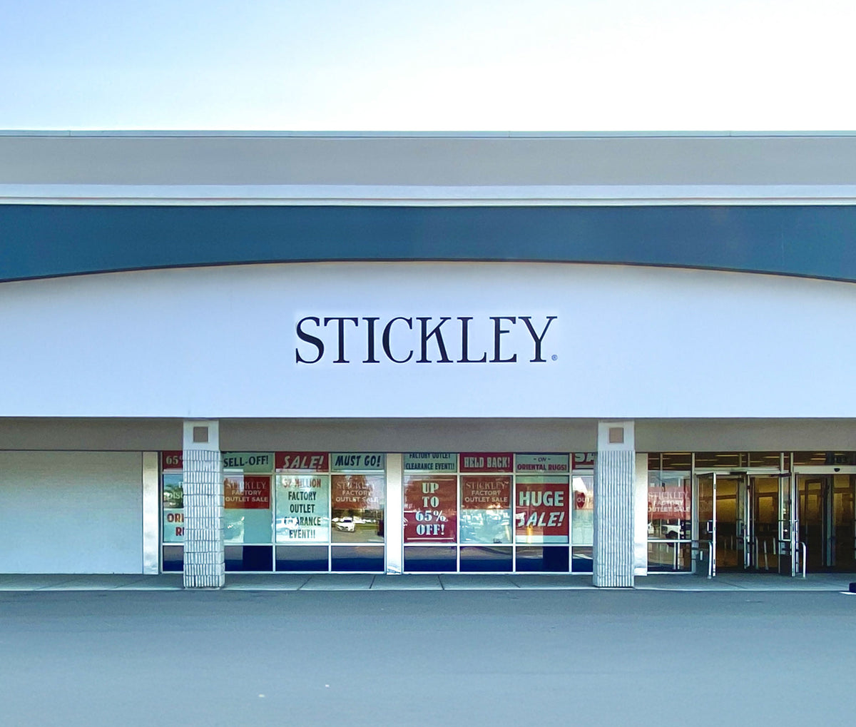 Exterior view of the Stickley Factory Outlet store in Buffalo, NY, featuring large sale signage promoting up to 65% off fine furniture and rugs.