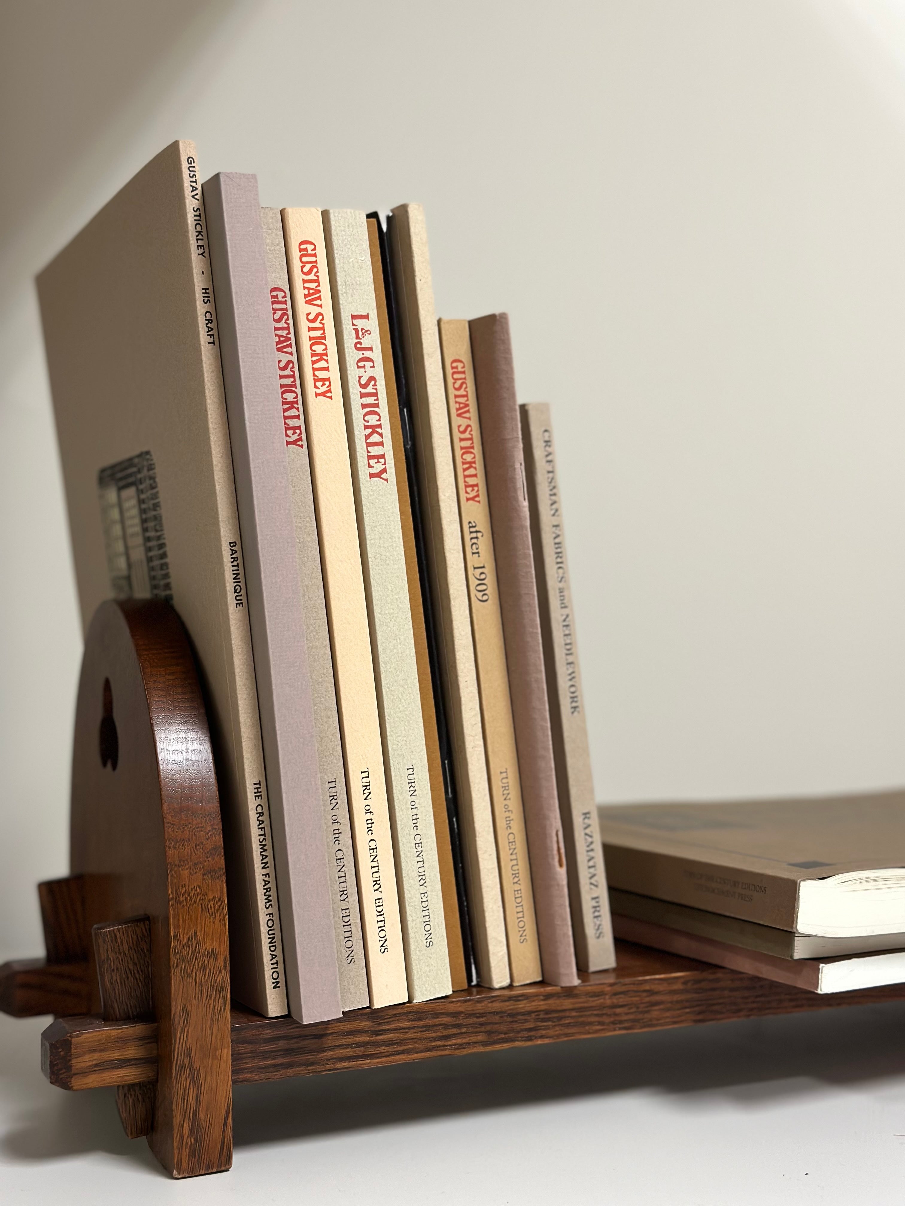 Bookshelf with a collection of books on Gustav Stickley and L. & J.G. Stickley, displayed on a wooden book rack in Mission-style design, featuring titles from Turn of the Century Editions and The Craftsman Farms Foundation.