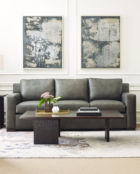 Origins by Stickley gray leather sofa with two gray and white paintings behind it and a dark brown coffee table in front.
