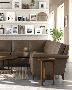 Origins by Stickley brown leather sectional, showcasing the corner of the sectional against a wall lined with shelving holding picture frames.