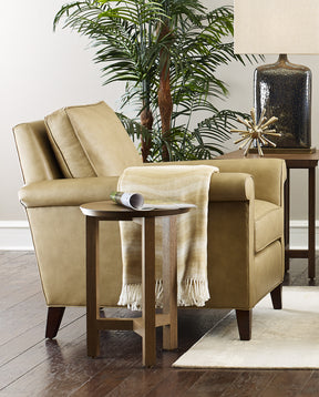 Origins by Stickley tan colored chair with dark brown legs, a yellow and white blanket draped over it's arm, and a brown end table beside it.