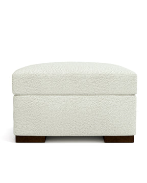 An Origins by Stickley white ottoman with dark wood legs against a white background.
