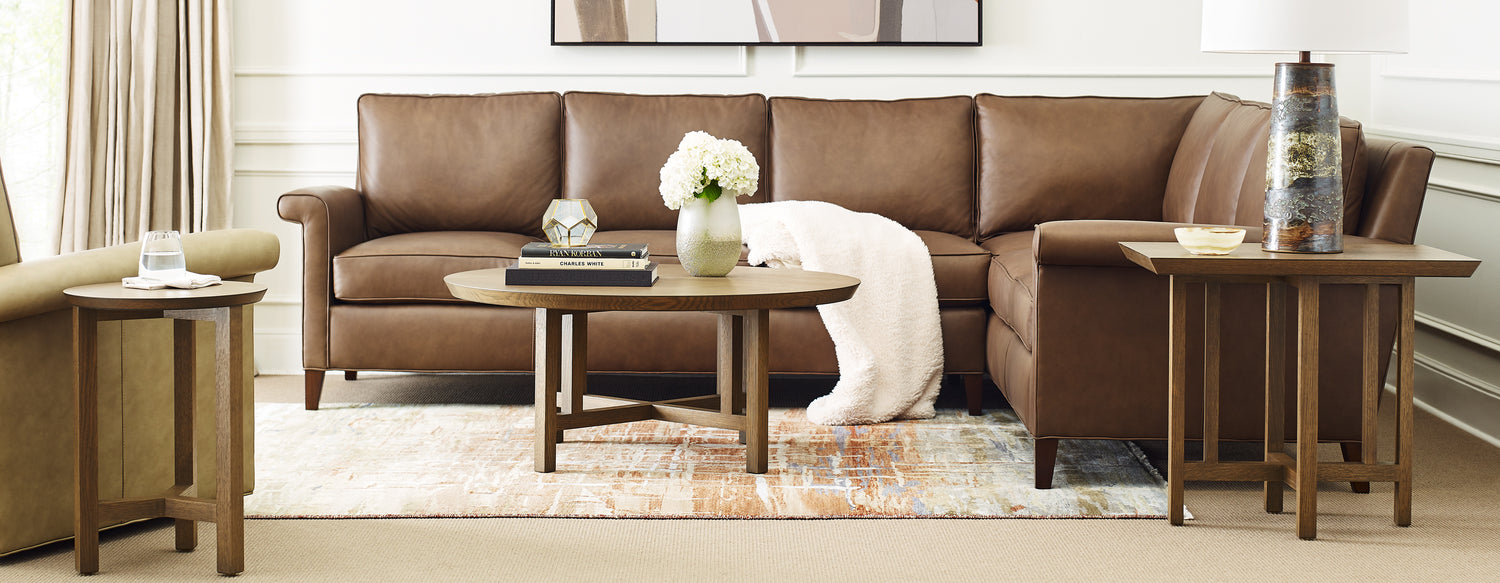 Origins by Stickley Keene brown leather couch draped with white blanket with a coffee table in front and two end tables.