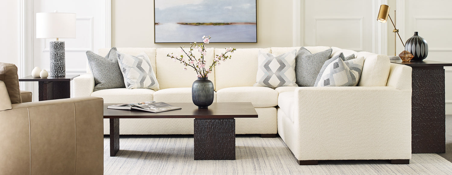 Origins by Stickley Keene white sectional with gray and white accent pillows and a dark brown coffee table in front.