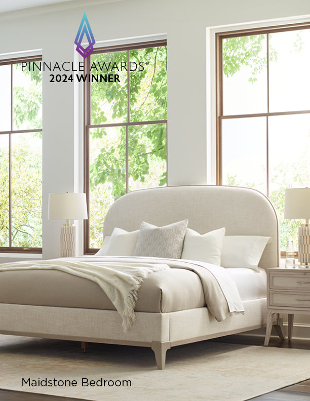 Bright and serene bedroom featuring the award-winning Maidstone Bed, with an upholstered headboard and frame in soft beige fabric, layered neutral bedding, matching nightstands with modern table lamps, and large windows letting in natural light; text overlay reads “Pinnacle Awards® 2024 Winner.”