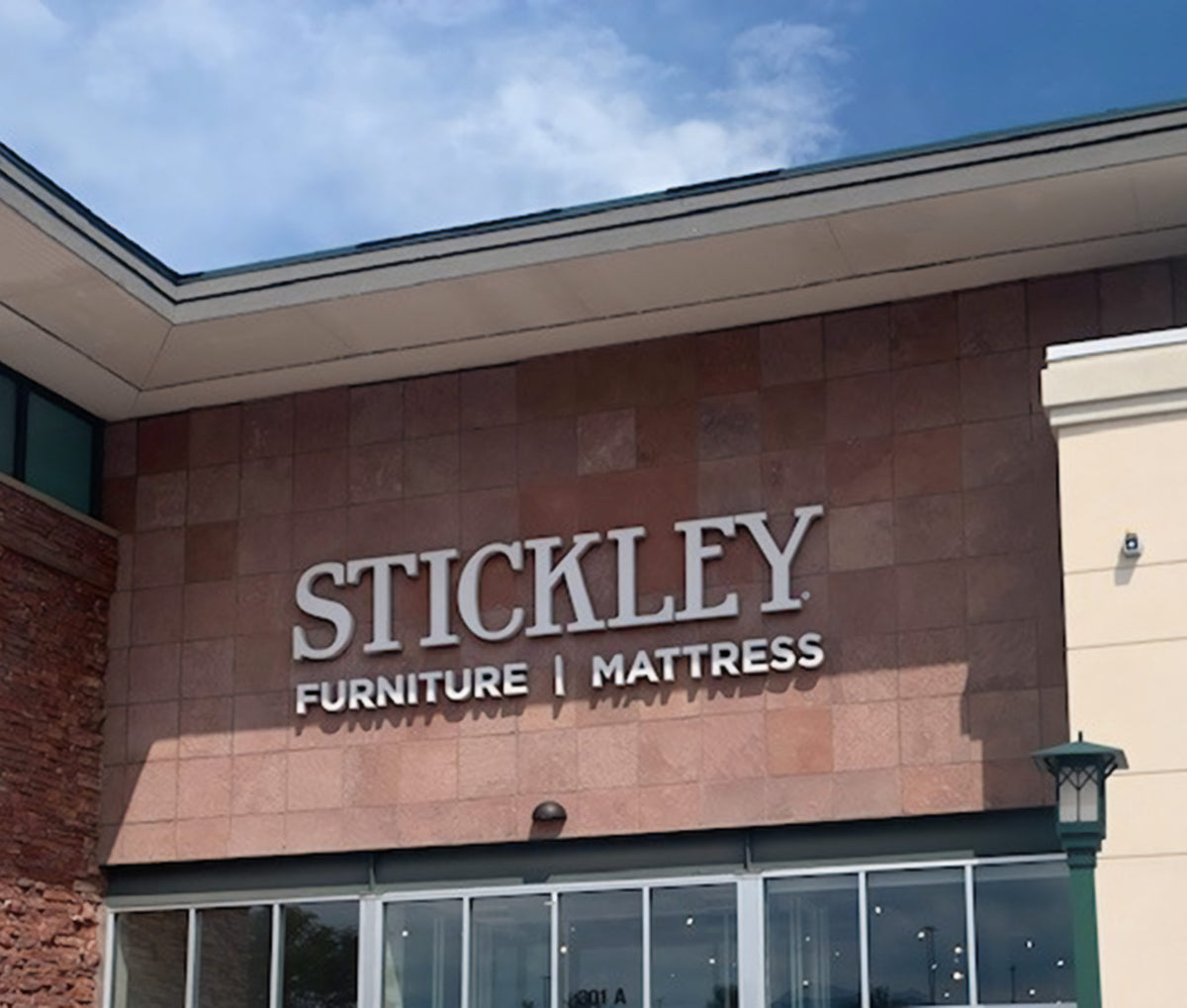 Exterior view of the Stickley Furniture & Mattress showroom in Superior, Colorado, featuring bold signage on a stone-tiled facade above glass entry doors—showcasing a destination for premium handcrafted furniture and luxury mattresses.