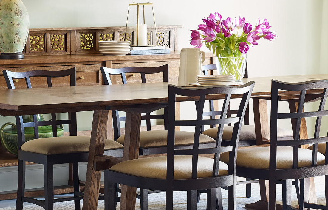 Lifestyle of Surrey Hills Trestle Dining Table, six side chairs, and two arm chairs with a Server with Gallery behind them against a light green wall