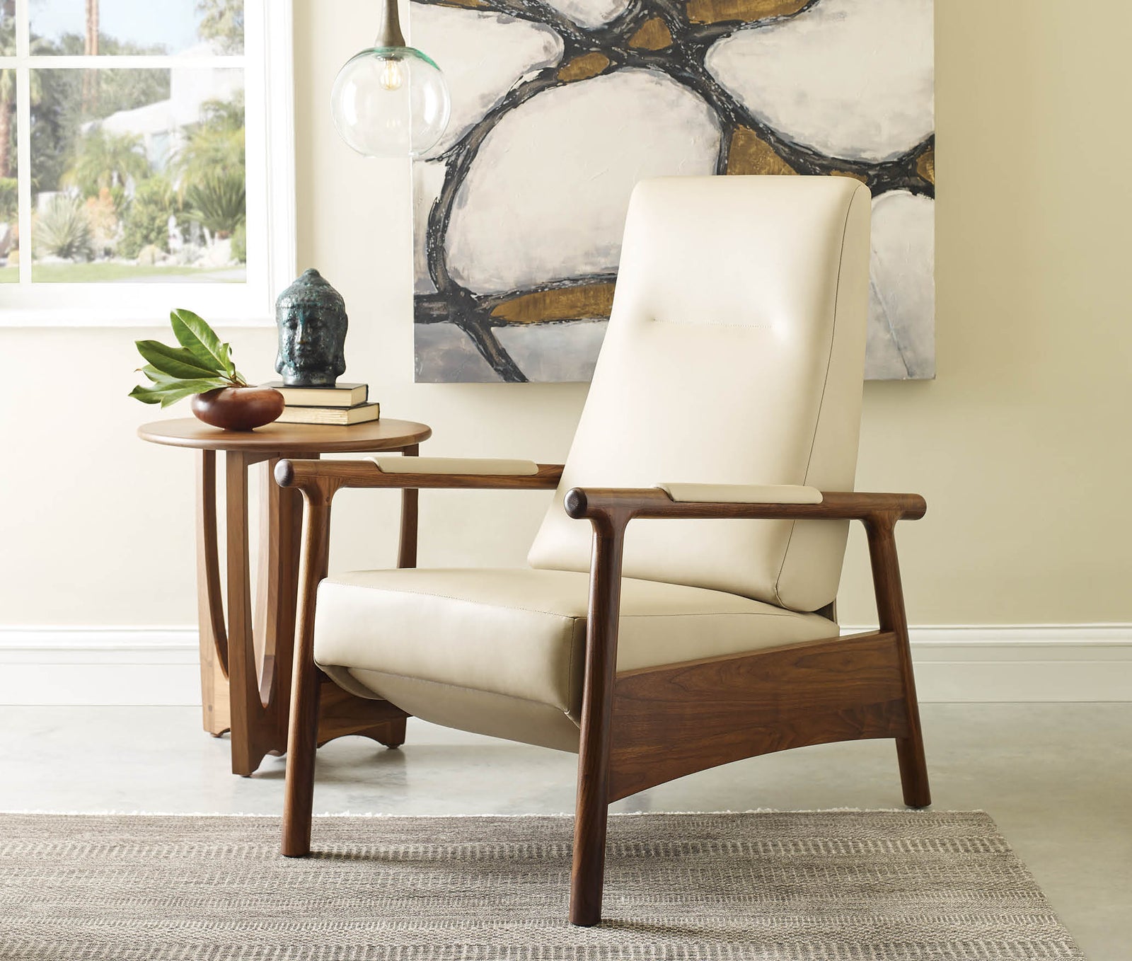Stickley Walnut Grove Recliner with a sculpted solid walnut frame and smooth ivory leather upholstery, featuring mid-century modern lines, angled arms, and a sleek silhouette, shown beside a matching walnut side table in a sunlit room with abstract art and a neutral area rug.