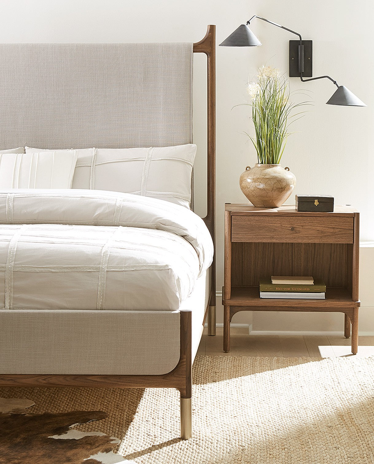 Walnut Grove nightstand and light gray upholstered bed that is cropped to only show half of the bed on top of a tan rug